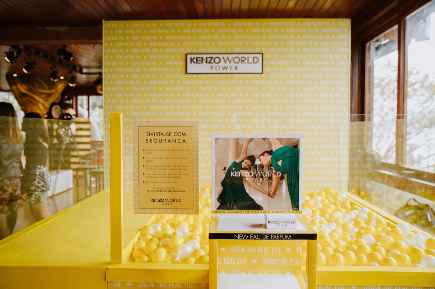 Yellow installation with a ball pit and a "KENZO WORLD POWER" sign in a room with a wood ceiling