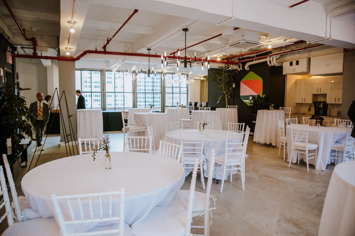 Hall with round tables in white tablecloths, white chairs, hanging chandeliers and large windows in the background