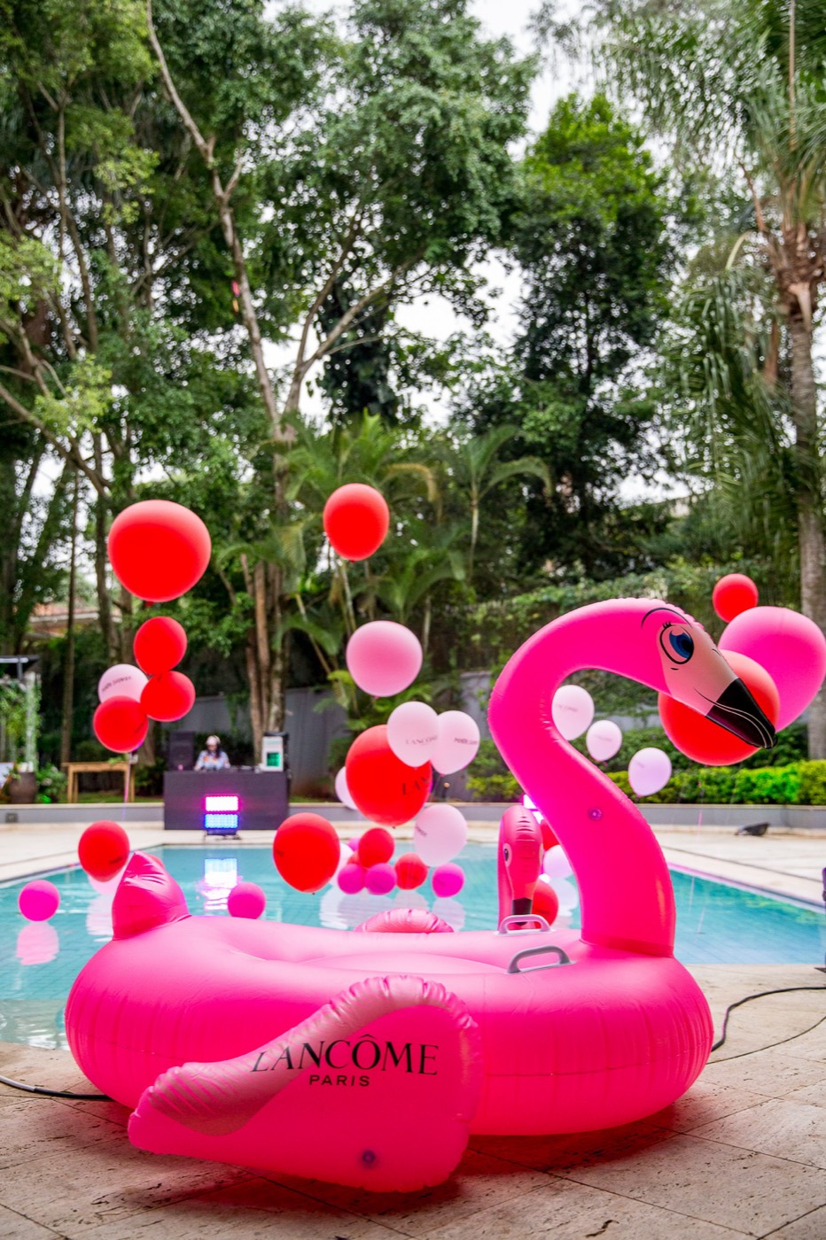 Giant pink flamingo float bearing "LANCÔME PARIS" at the edge of a pool with red and pink balloons