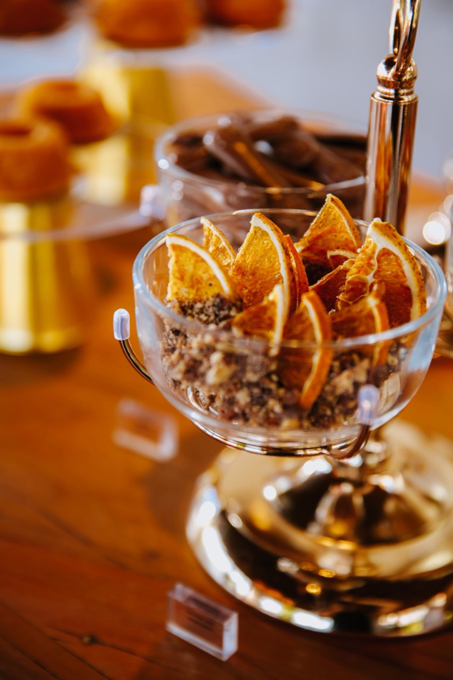 Glass bowl with dried orange slices on a wooden table, with sweets in the background