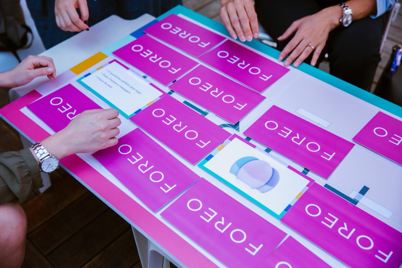 Several people's hands over a table with magenta cards reading "FOREO" arranged in rows