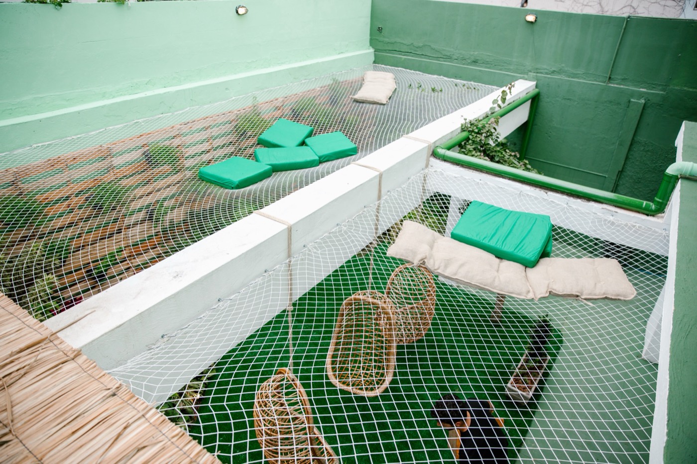Suspended nets with green cushions over an opening, seen from above, with wicker pieces on the floor below
