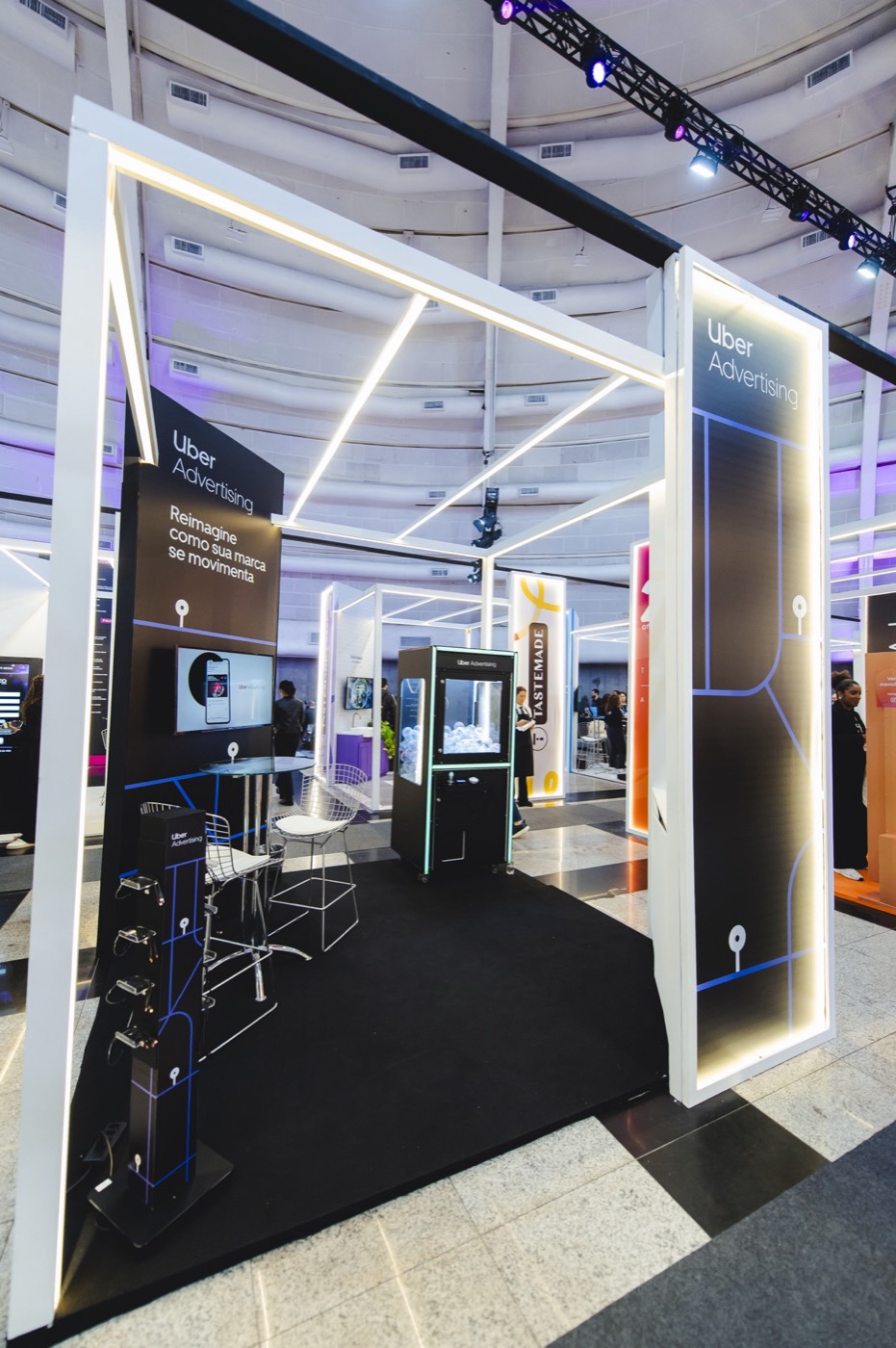 Booth with white light frames, black carpet, "Uber Advertising" panels and a lit display case in the center
