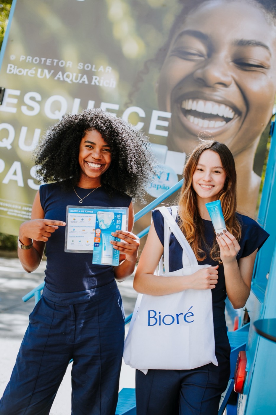 Two people smile in front of the truck panel, showing a flyer and a product, with a "Bioré" tote bag