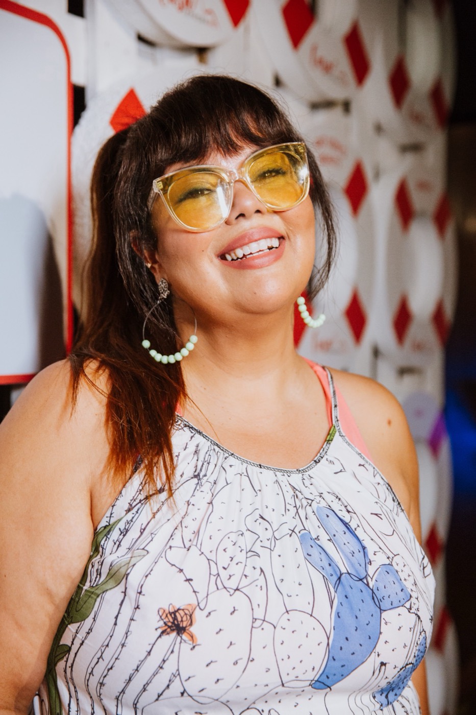 Smiling person in yellow glasses and a printed dress in front of a wall of white and red life rings