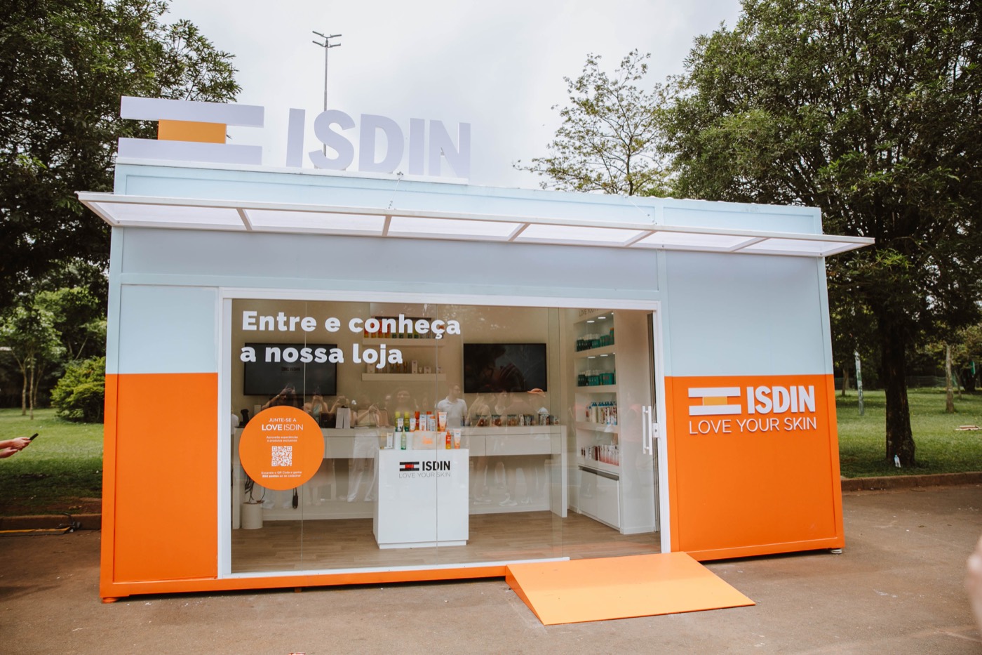 Facade of a white and orange container store with a glass front, access ramp and "ISDIN" sign on top
