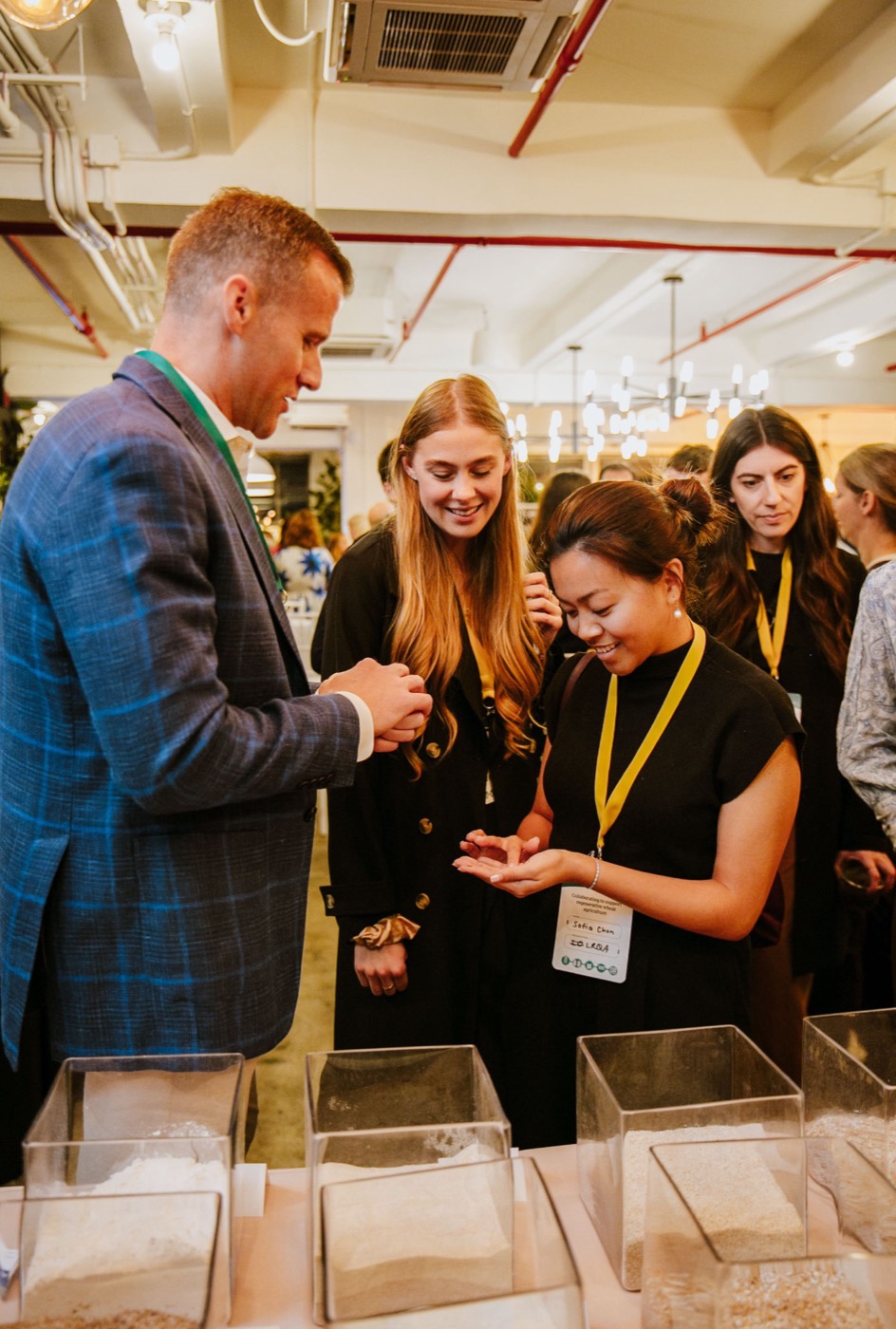 People wearing badges examine grain samples in their hands in front of acrylic boxes on the table