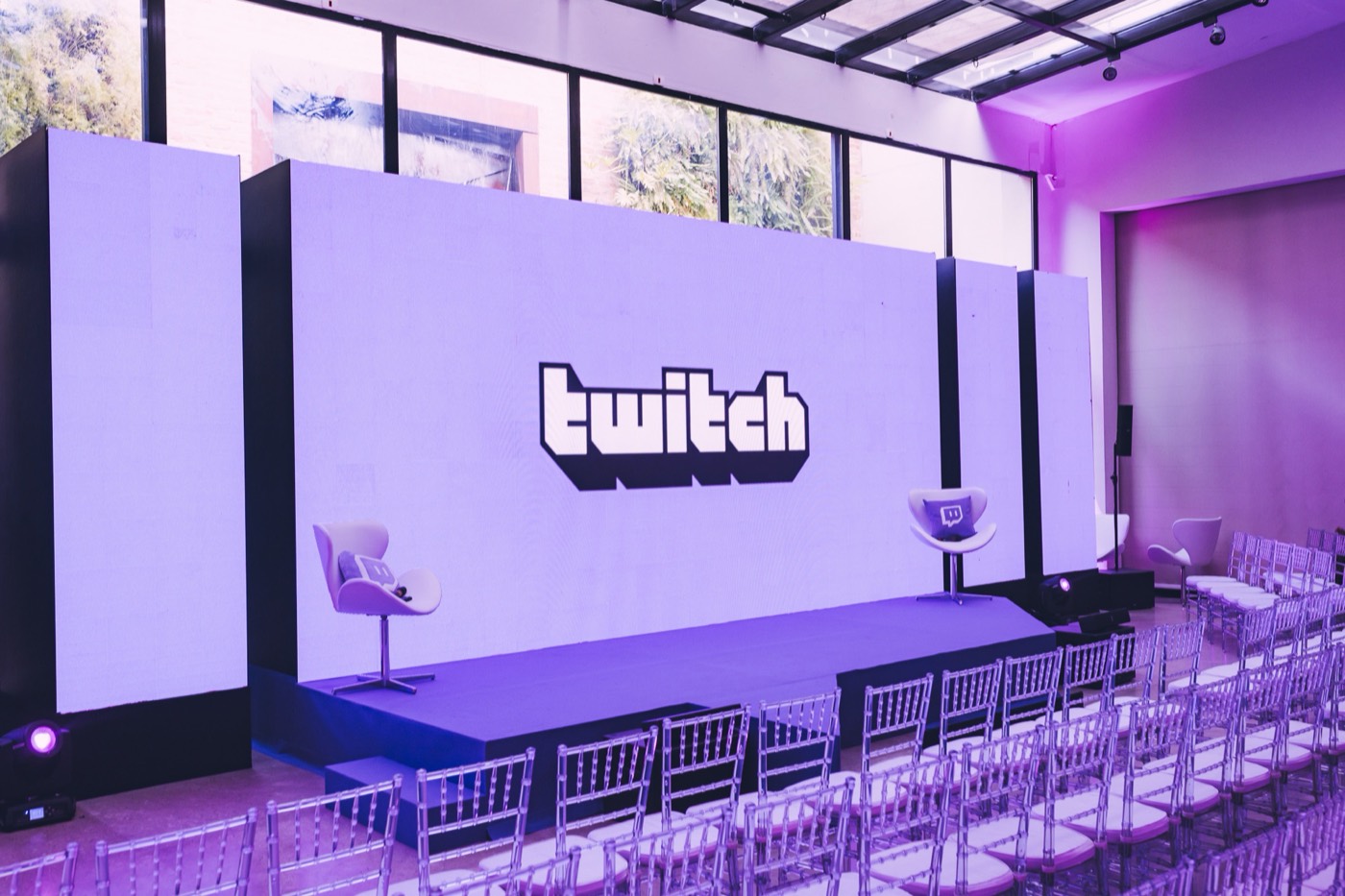 Empty stage with an LED panel showing "twitch", two armchairs and rows of clear chairs