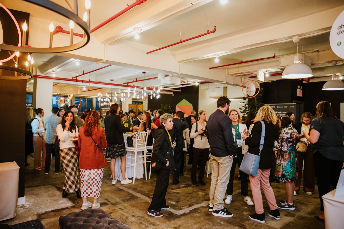 Hall full of guests standing and chatting, with pendant lamps and red pipes on the ceiling