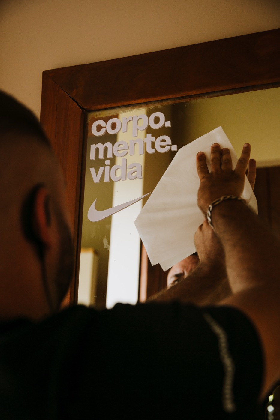 Person seen from behind presses a sheet with both hands onto a mirror bearing a "corpo. mente. vida" decal