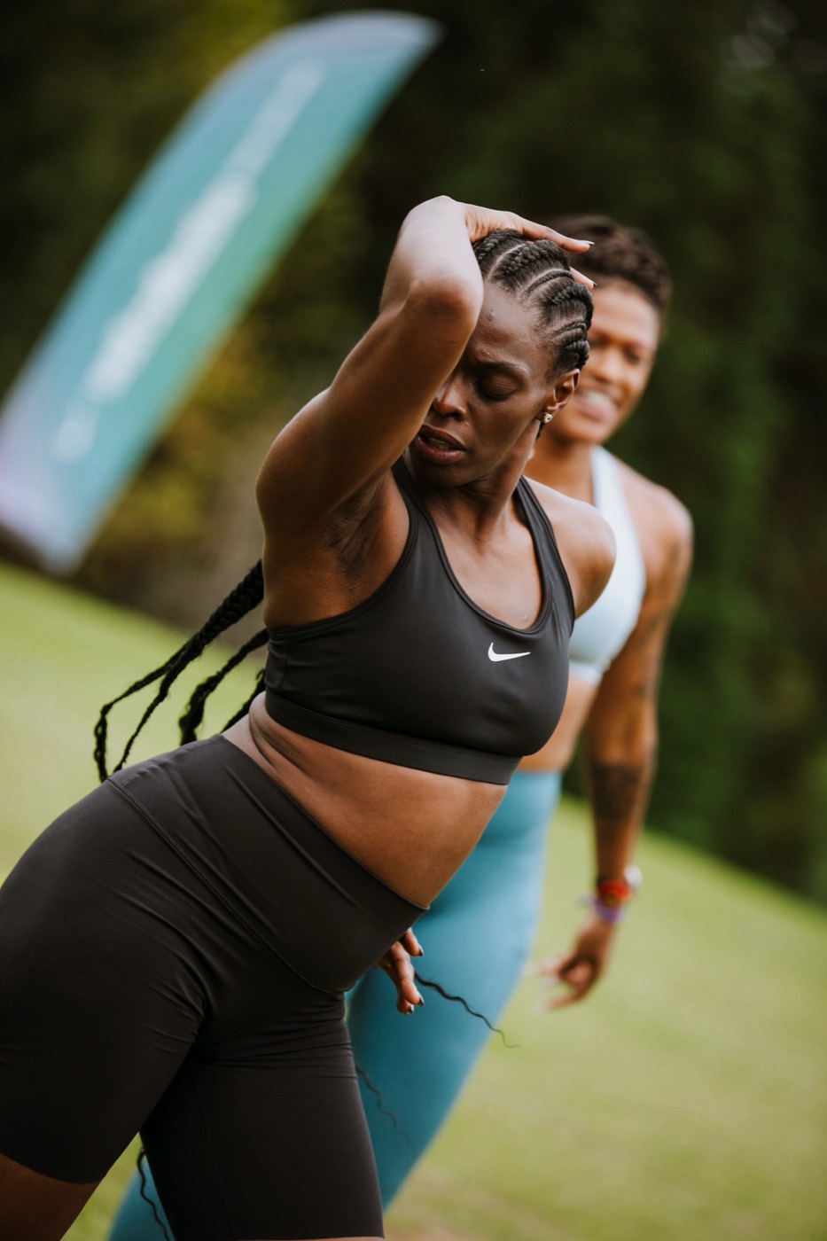 Two people in workout clothes move on a lawn, one of them with an arm raised over their head