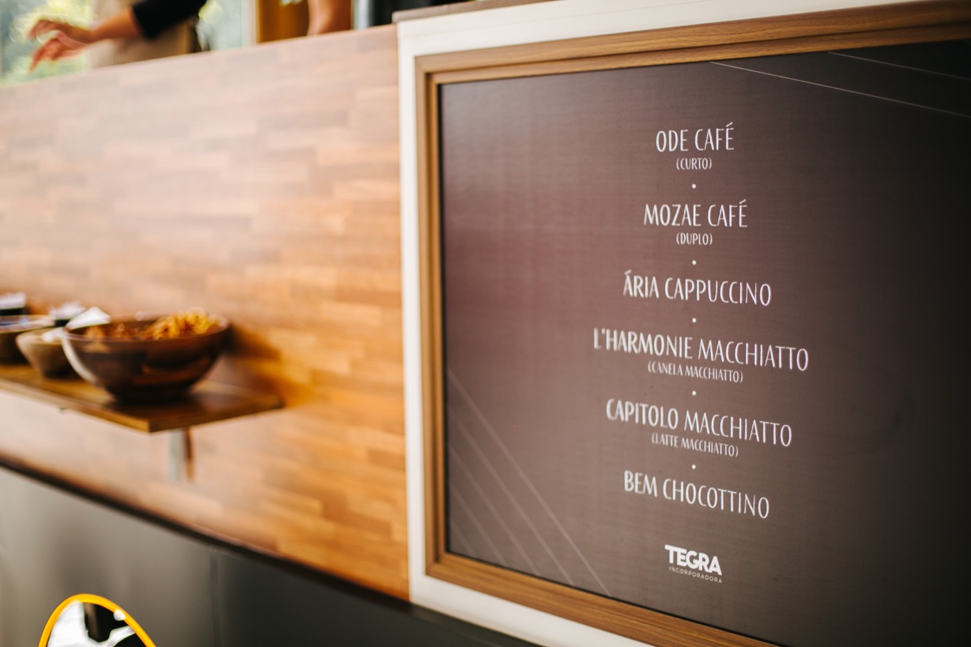 Dark menu board listing coffee drinks with a "TEGRA" logo on a wood-clad counter