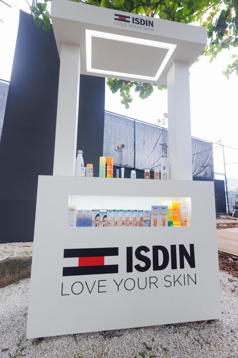 White display stand with products and the "ISDIN LOVE YOUR SKIN" logo in an outdoor gravel area