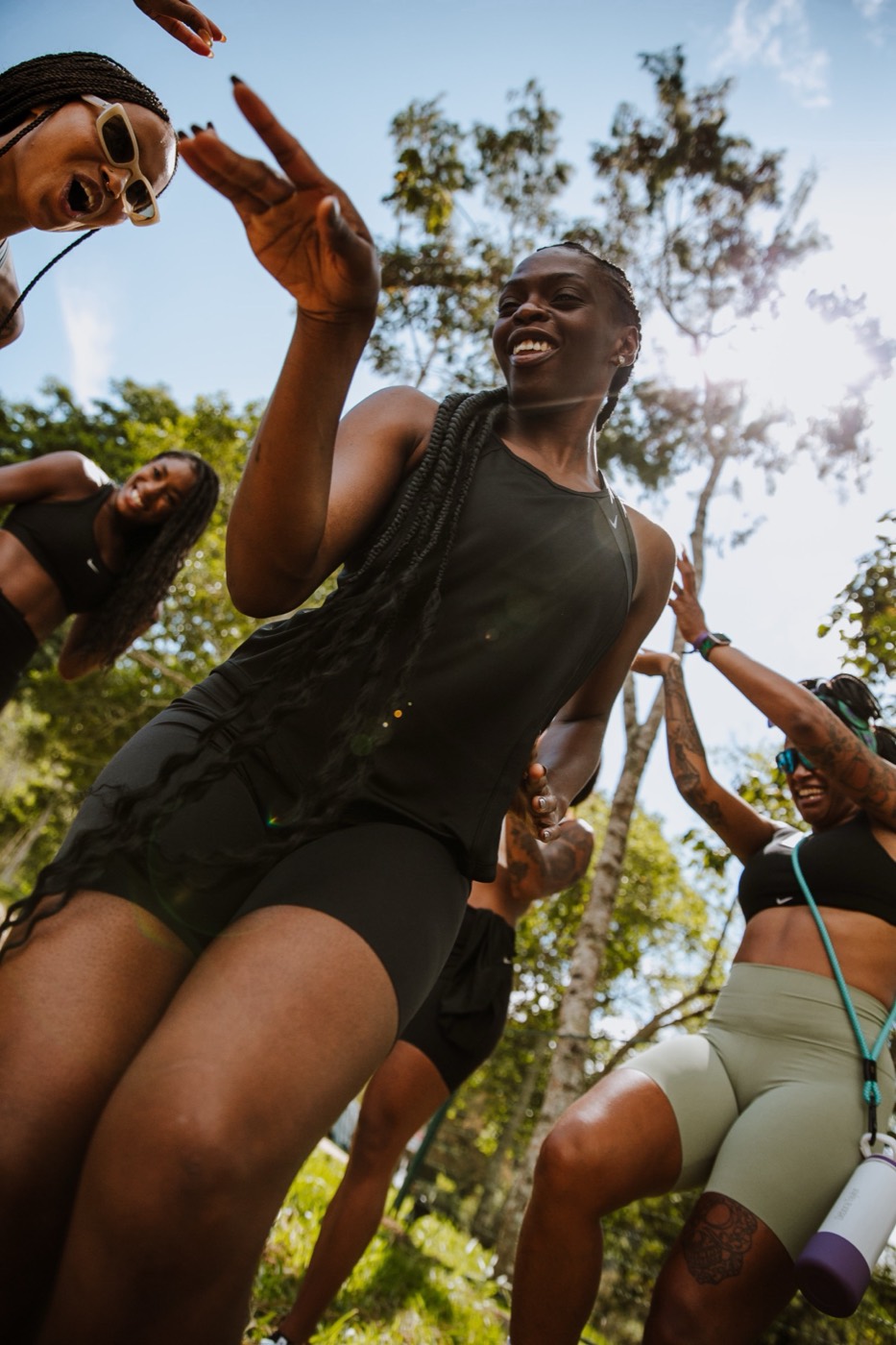 People in workout clothes smile and move outdoors, seen from below against the sky and trees