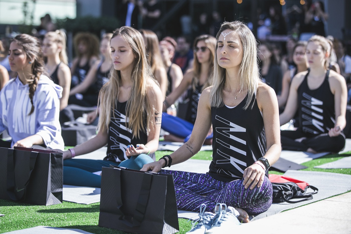 Participants seated cross-legged with eyes closed on mats outdoors, wearing black "NIKE" tank tops
