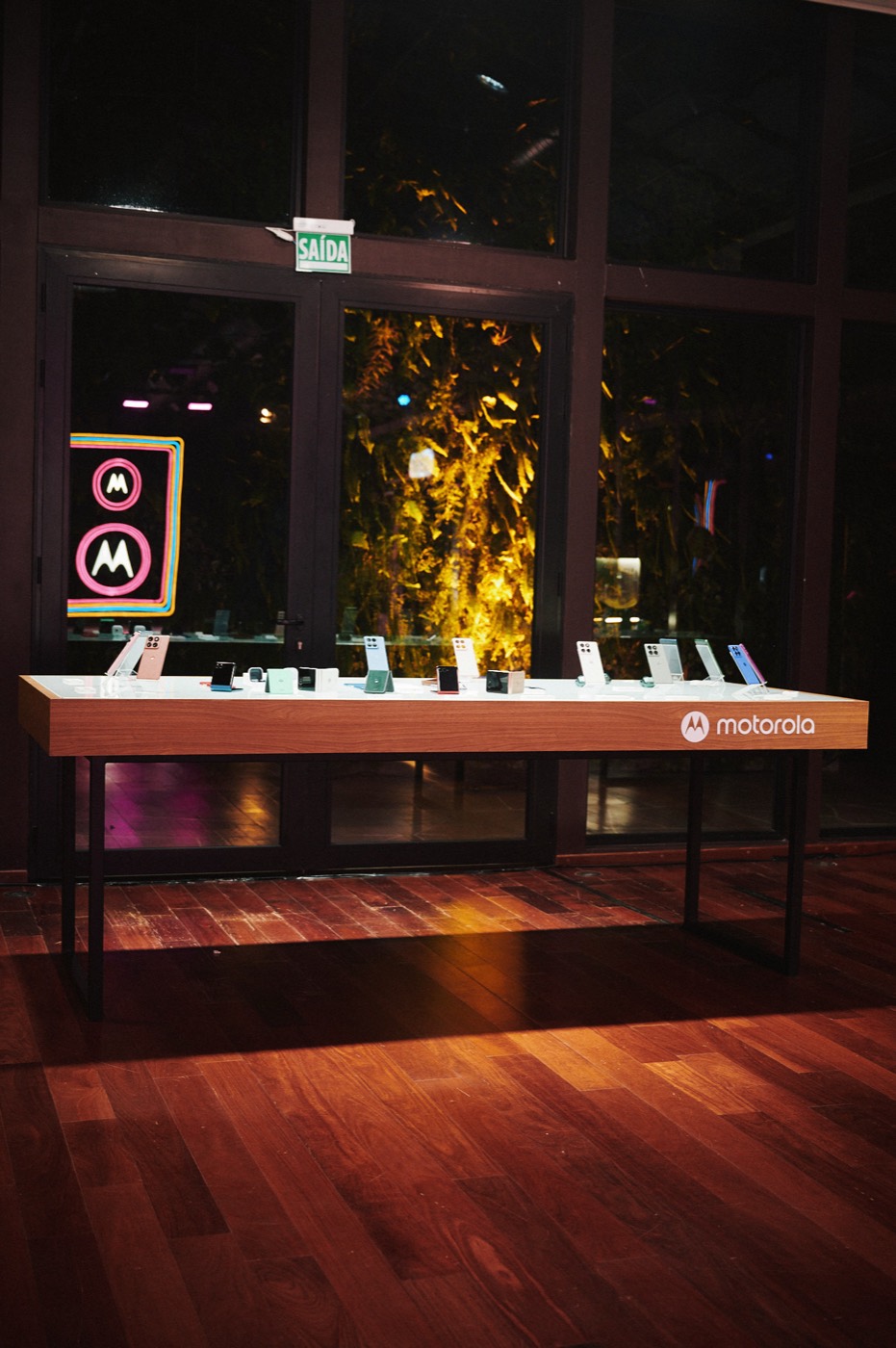 Wooden table displaying smartphones with a "motorola" logo, in front of windows facing a lit garden