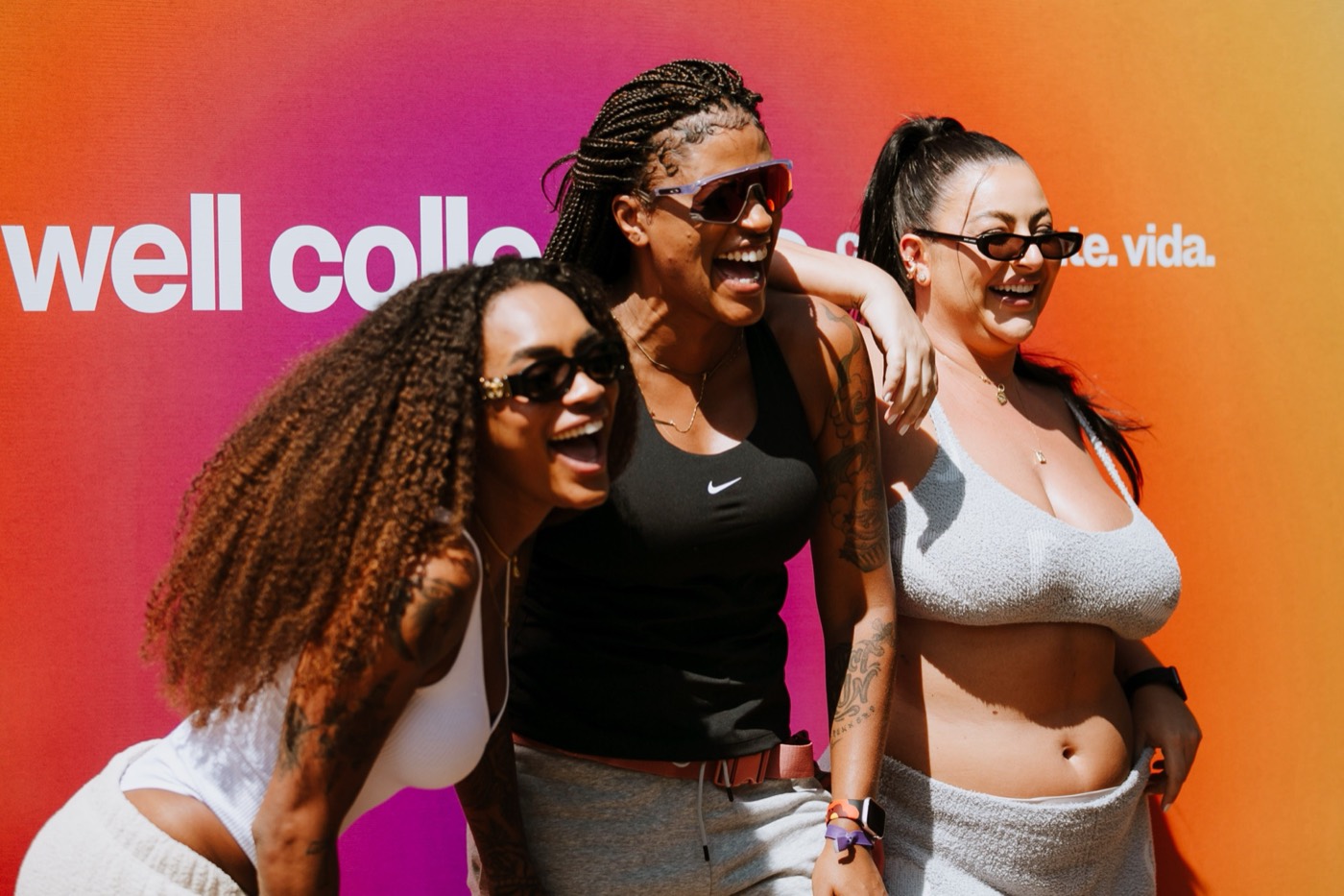 Three people laugh with arms around each other in front of a pink and orange gradient panel with white lettering