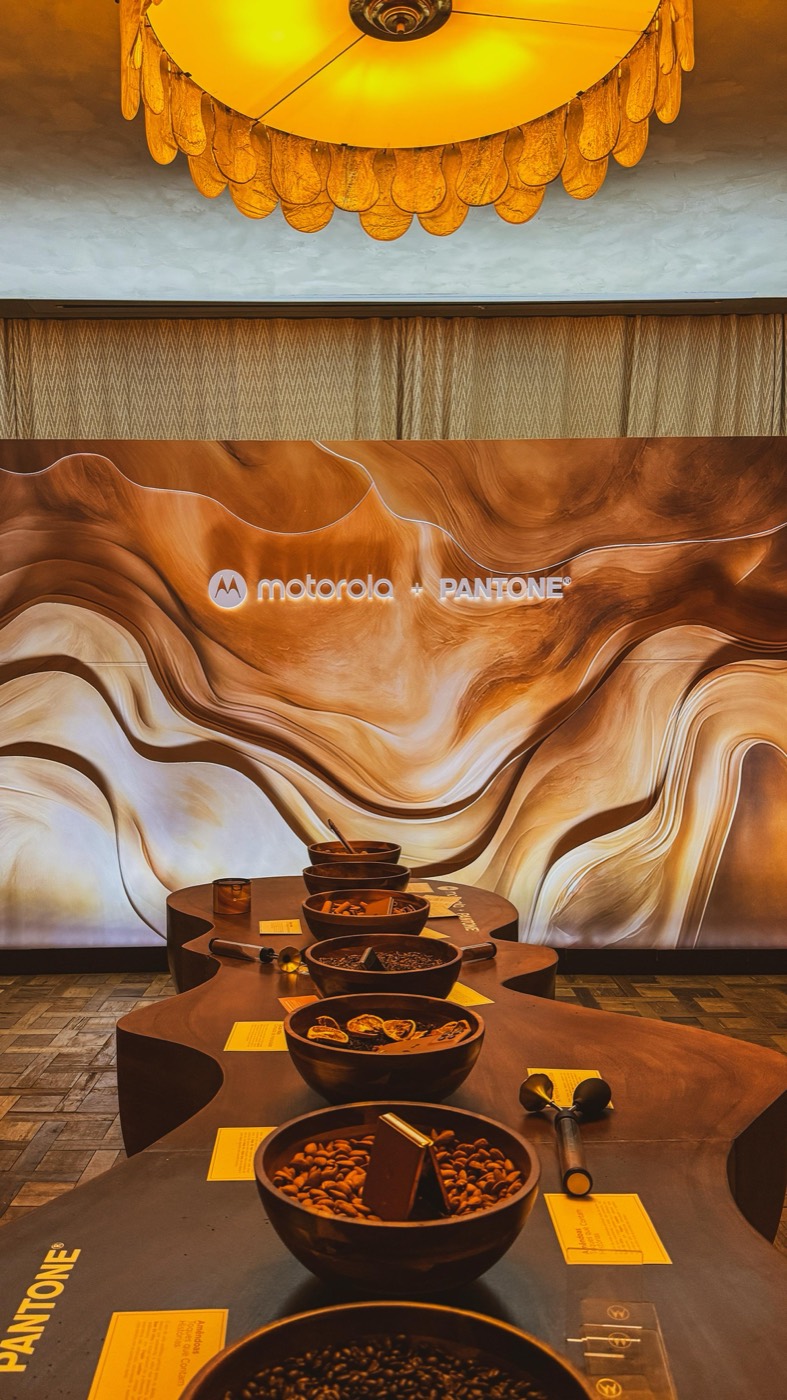 Backlit panel of brown-toned waves reading "motorola + PANTONE" behind a curved table with bowls of beans