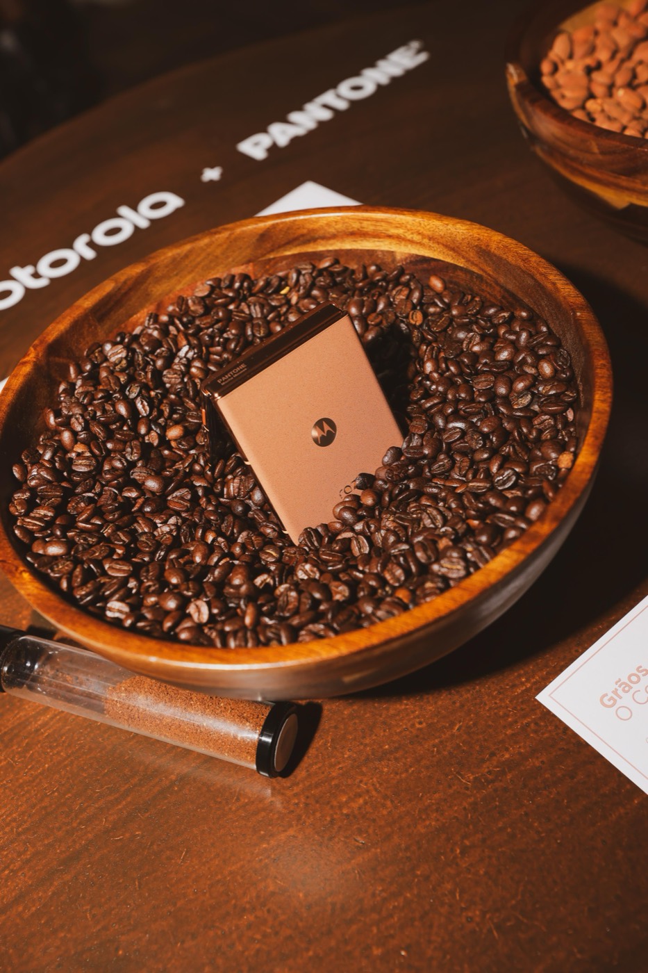 Light brown flip phone resting on coffee beans in a wooden bowl, next to a glass tube