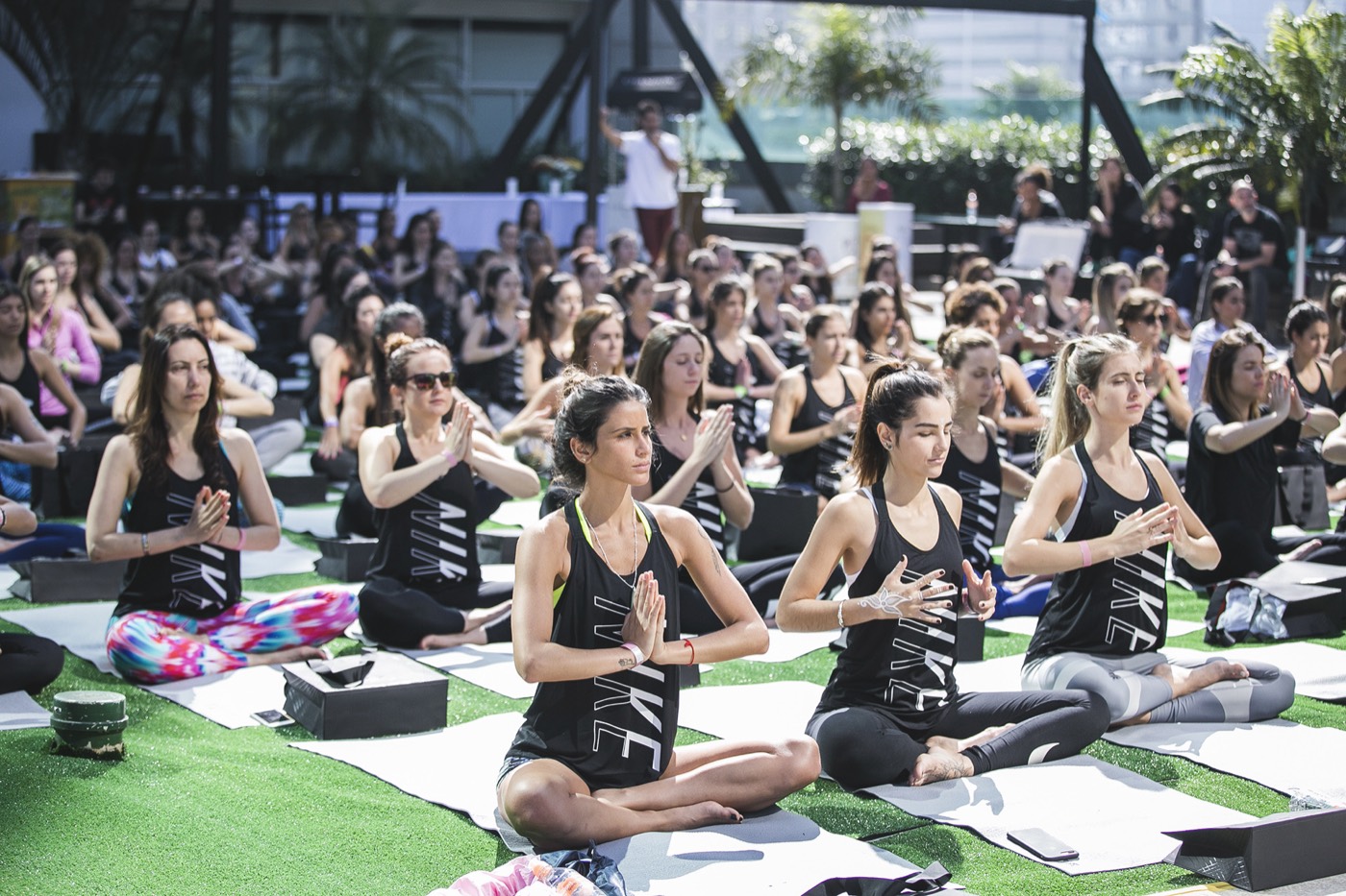 Participants seated cross-legged with hands joined at the chest in an outdoor class