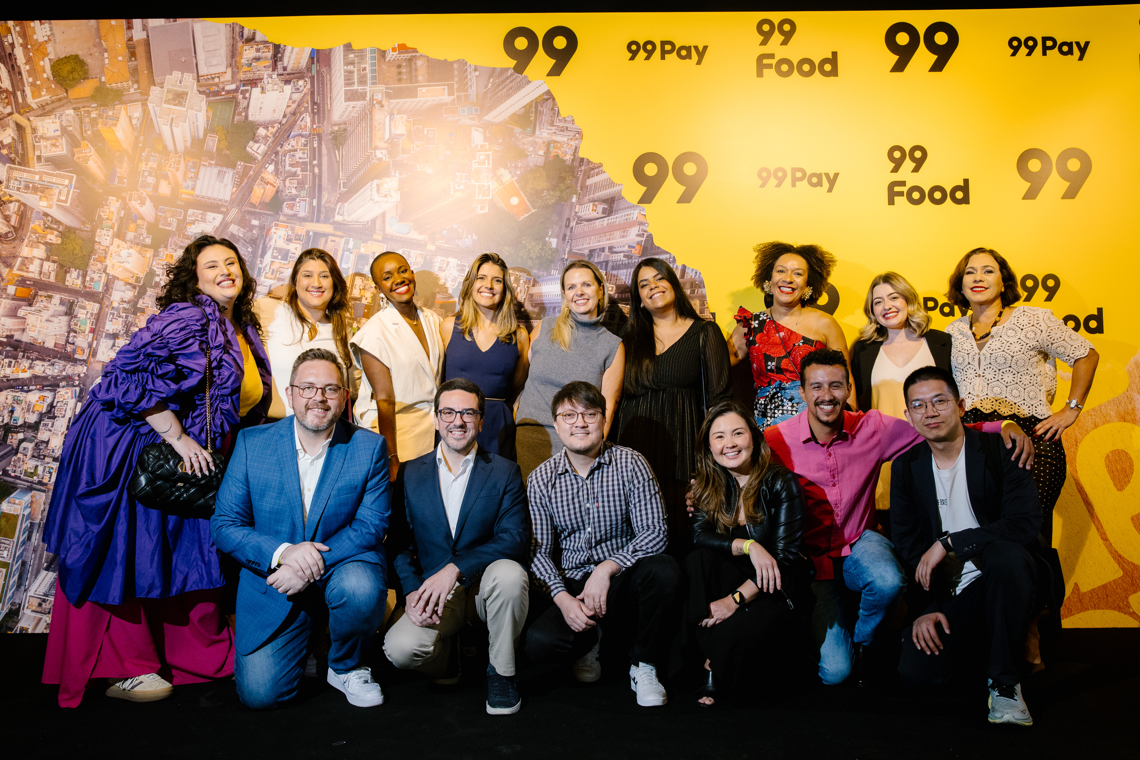 Group poses in front of a yellow panel with an aerial map and "99", "99Pay" and "99 Food" logos