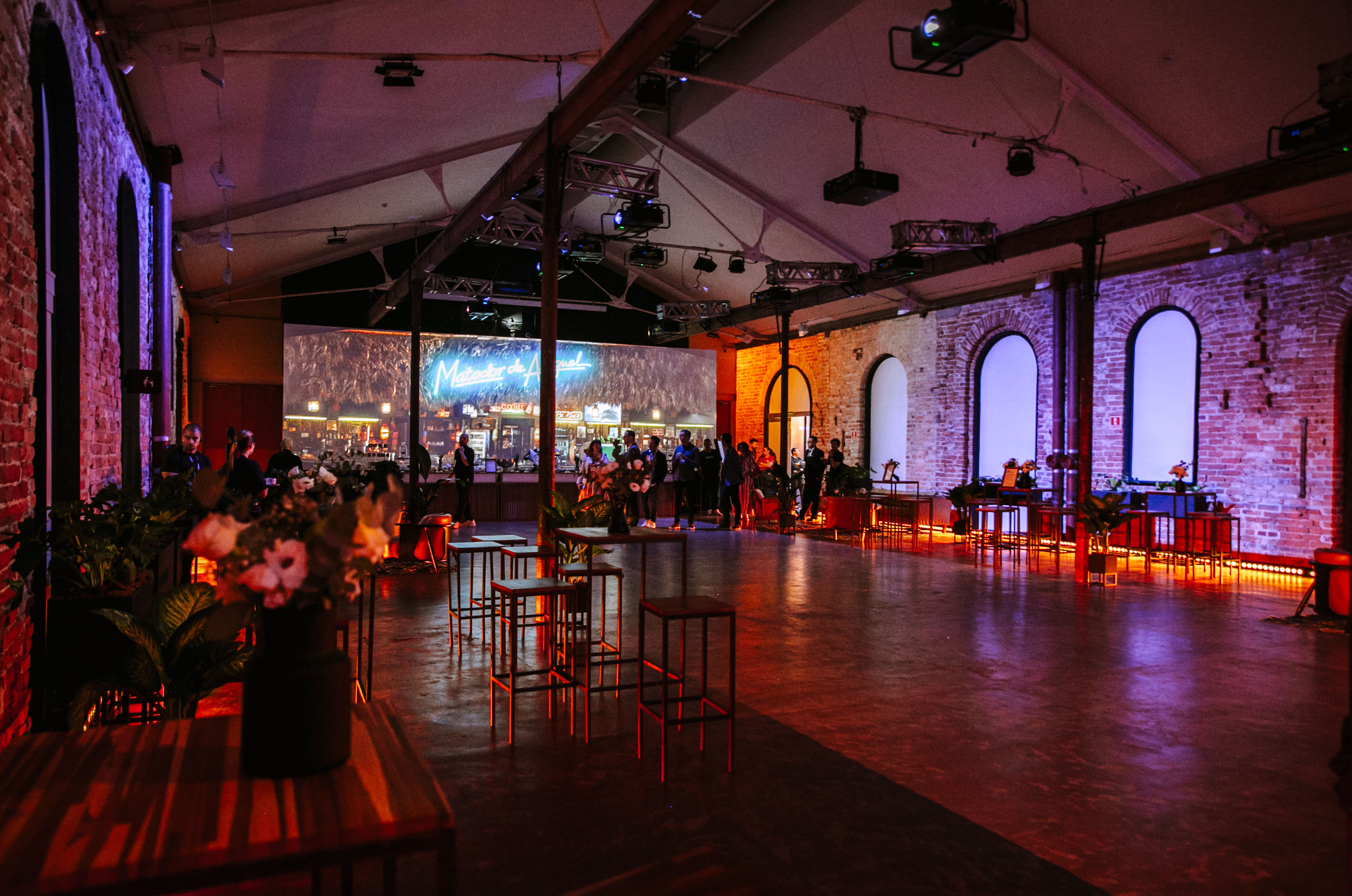 Brick hall with arched windows, high tables, flower arrangements and guests gathered in the background