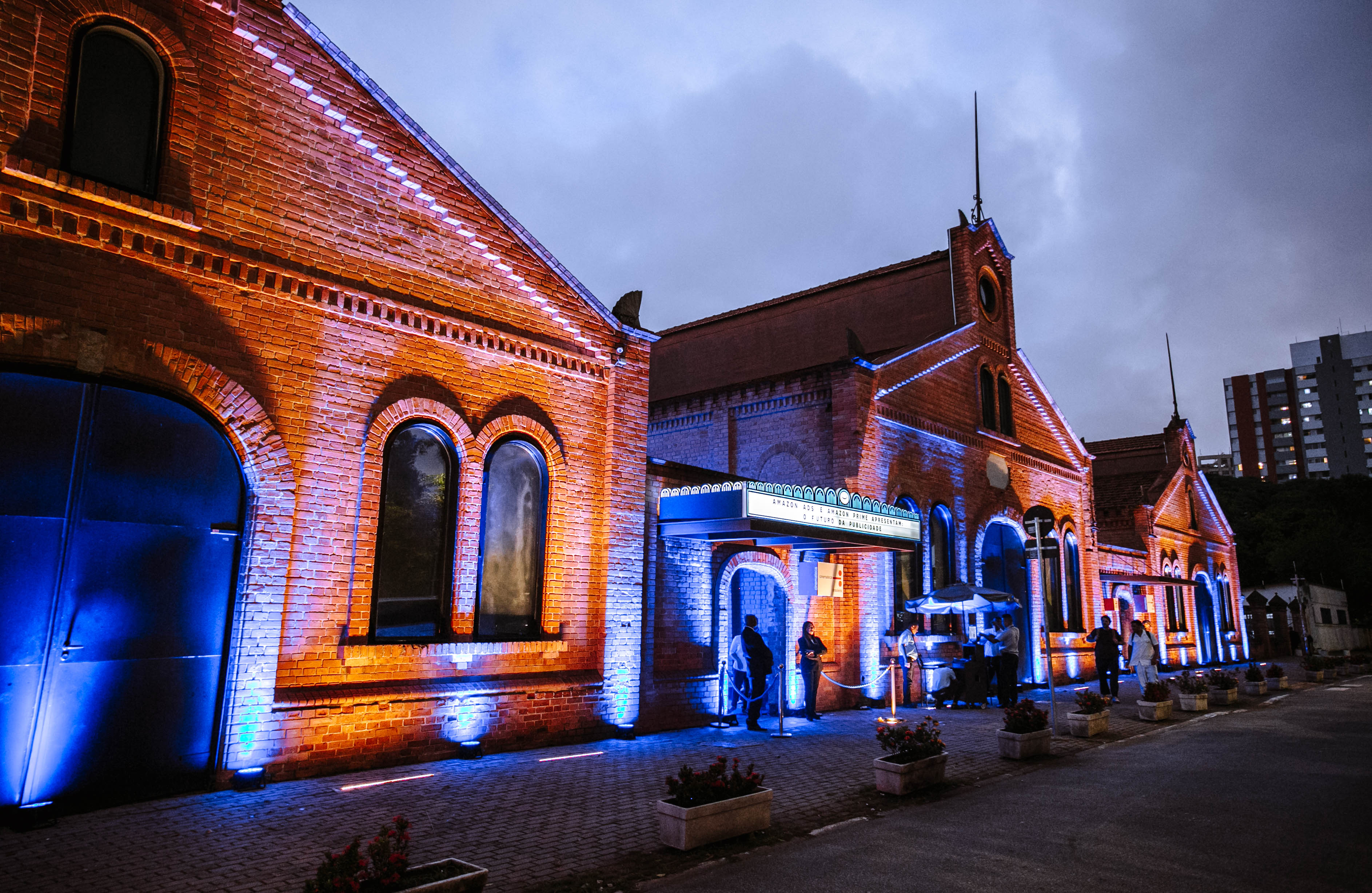 Brick warehouse facades lit in blue and orange at dusk, with people at the entrance